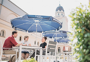 Drei junge Menschen sitzen im sonnendurchfluteten Hof der Jugendherberge Halle.