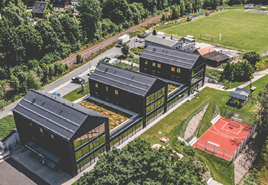 Ein Gebäudekomplex mit drei Giebelhäusern und einem Sportplatz