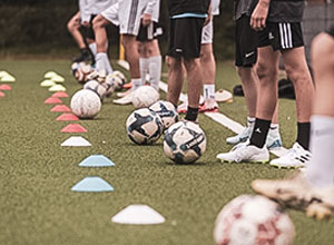 Man sieht die Beine von Fußballspielern, die auf einer Linie stehen und vor denen Fußbälle liegen