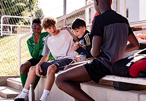 Jugendliche sitzen in Sportkleidung auf einer Tribüne und machen eine Pause beim Training.