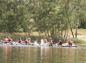 Kinder paddeln gemeinsam auf Flößen über einen See.