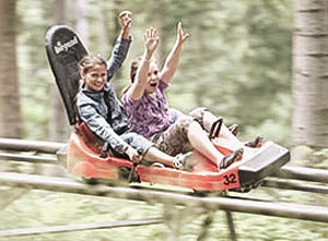Zwei Kinder fahren lachend mit einer Sommerrodelbahn.