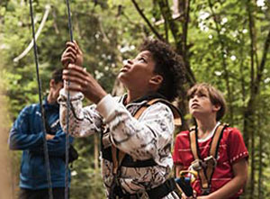 Kinder sichern sich gegenseitig beim Klettern im Wald.